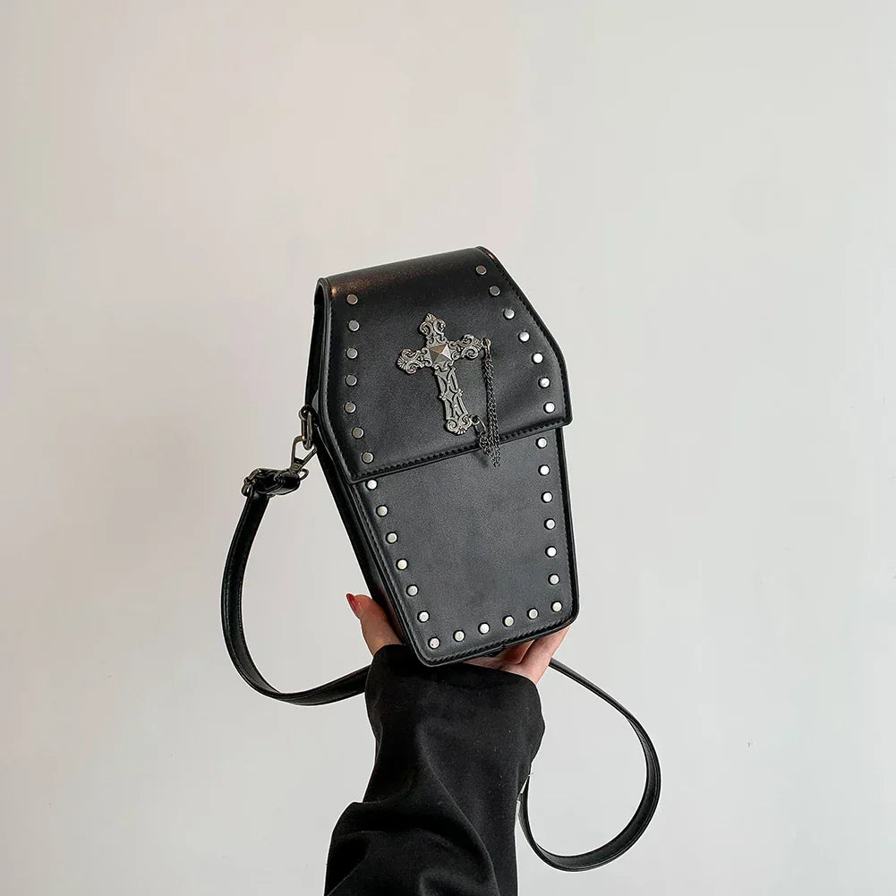 Midnight Edge Crossbody bag in luxury black vegan leather shaped like a coffin with silver cross embellishment and metal stud accents shown held by model showcasing bold gothic design durable premium construction and spooky chic upscale styling for alternative fashion lovers