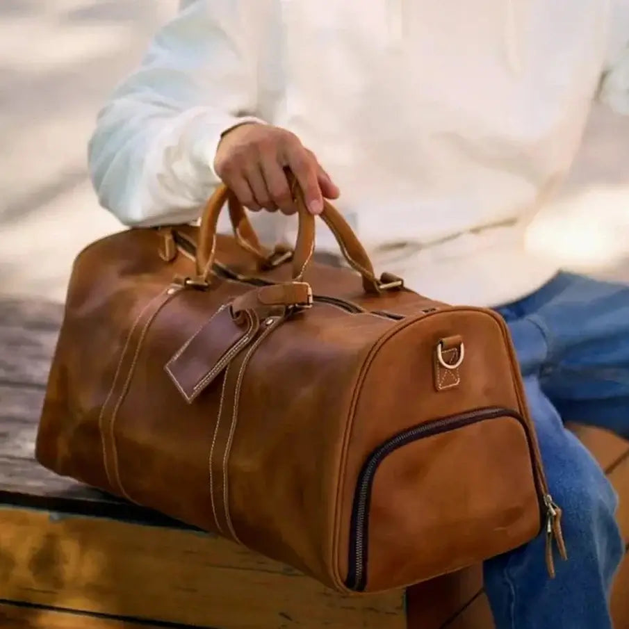 Heritage Leather Weekender in luxury brown thick vintage genuine leather with structured duffel silhouette dual top handles zipper closure and attached tag held by model showcasing classic craftsmanship upscale styling and premium timeless travel functionality
