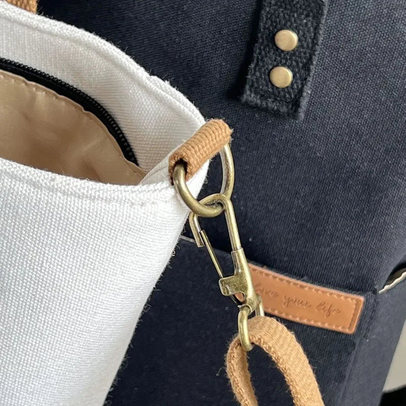 Beige Timeless Canvas Carry tote close up of brass crossbody clasp and black Timeless Canvas Carry tote with leather logo tag premium womens canvas totes