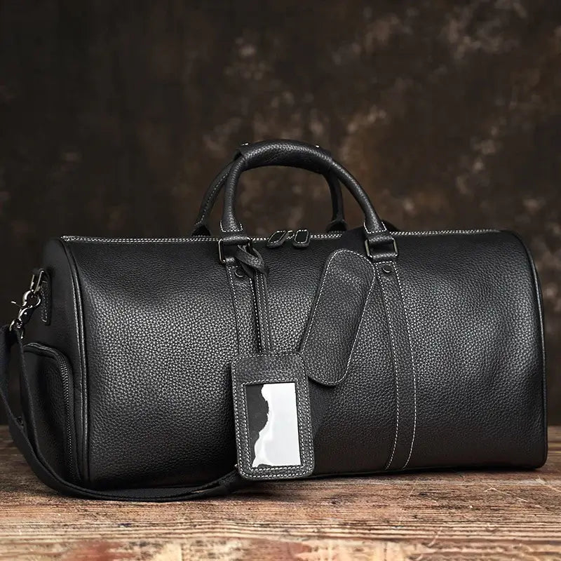 Heritage Leather Weekender in black thick vintage luxury genuine leather with cylindrical silhouette dual top handles detachable adjustable shoulder strap and white luggage tag showcasing classic premium craftsmanship rich patina upscale detailing and timeless travel aesthetic