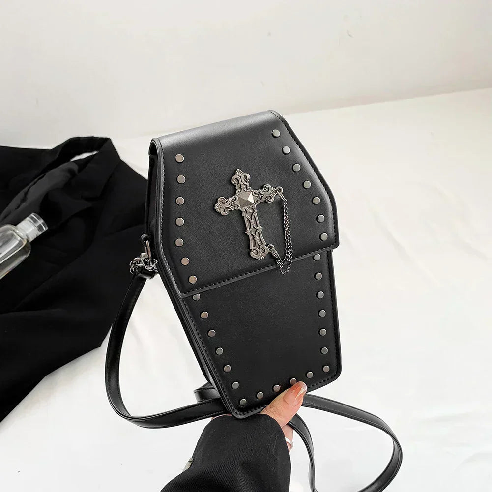 Midnight Edge Crossbody bag in black luxury vegan leather shaped like a coffin with silver cross embellishment and metal stud accents shown held by hand over white surface featuring flap closure and adjustable strap showcasing bold unconventional design and durable premium construction for upscale gothic inspired styling
