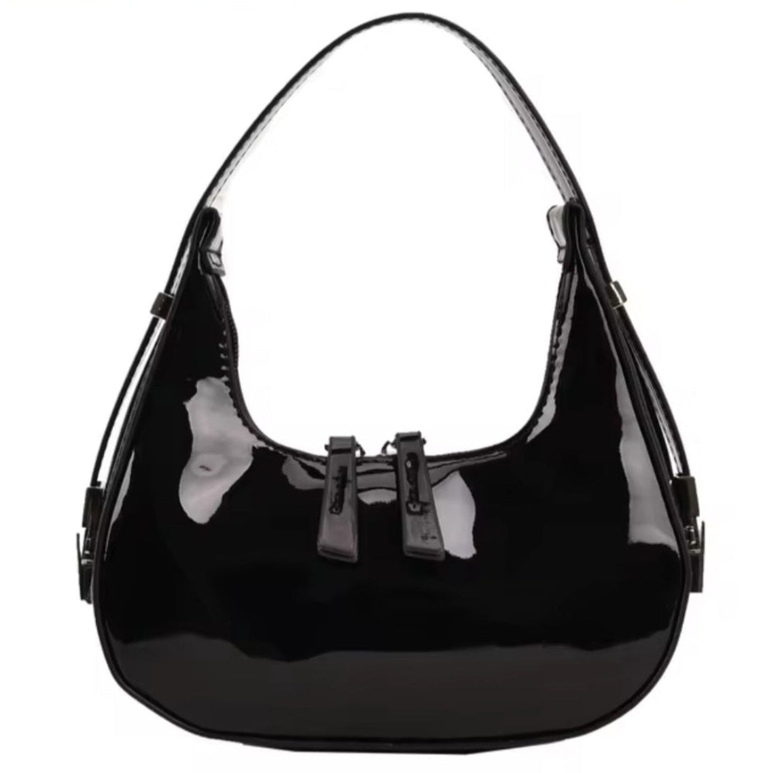 Luna Curve Carry luxury bag in glossy black vegan leather with crescent silhouette single shoulder strap front bow accent and silver hardware displayed showcasing bold modern styling polished premium finish and compact everyday elegance