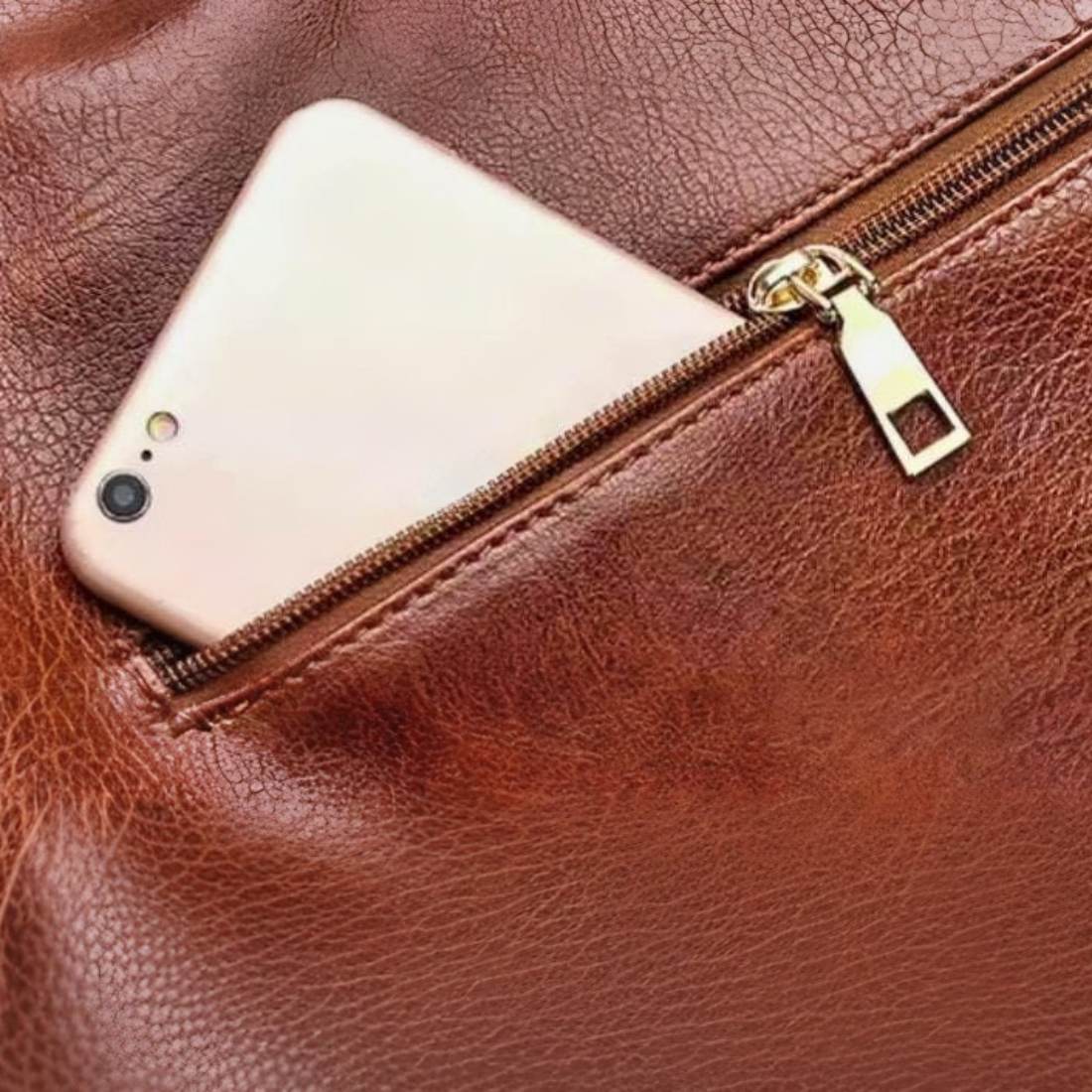 Classic Carry Hobo in brown premium vegan leather showing elegant gold tone zipper partially open with white smartphone tucked into back pocket showcasing secure storage upscale detailing and practical everyday luxury design