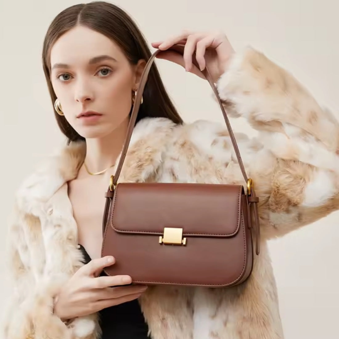 Timeless Charm Satchel in caramel genuine kitt cross grain leather with structured rectangular silhouette flap front design gold accent hasp closure and short shoulder strap held by model showcasing luxury styling upscale craftsmanship premium finish and compact everyday sophistication
