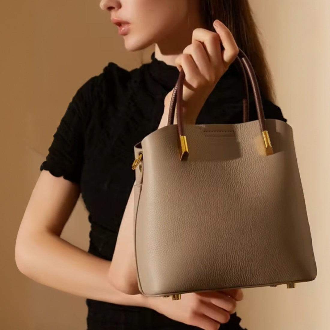 Luxe Bucket Carry beige luxury genuine leather handbag with upscale gold hardware held by model in black top showcasing elegant handheld carry style