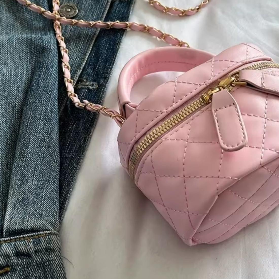 Timeless Petite Luxe elegant crossbody bag in pink quilted vegan leather with upscale gold zipper and elegant gold chain strap compact silhouette placed beside blue denim jeans on white surface showcasing luxury design in lifestyle setting