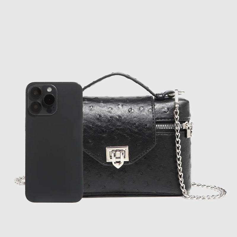 Timeless Petite Luxe women’s black vegan leather crossbody bag with silver chain strap and phone shown for scale