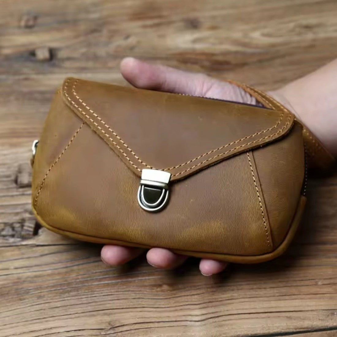 Heritage Utility Carry in retro brown crazy horse genuine leather with distressed oil wax finish compact structured silhouette with triangular flap visible stitching and antique brass clasp held by hand showcasing vintage charm and upscale craftsmanship